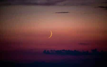 A crescent is seen in the sky at sunset