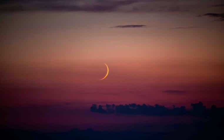 A crescent is seen in the sky at sunset