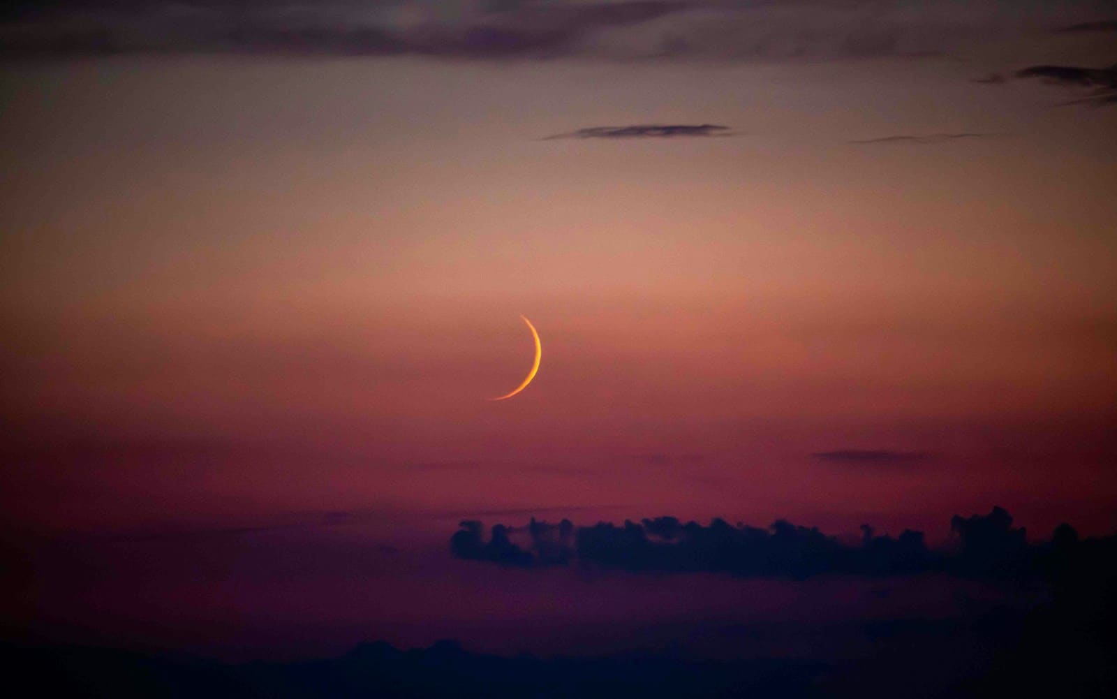 A crescent is seen in the sky at sunset