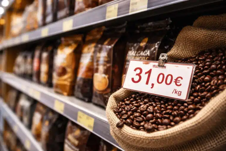 Prix du café en hausse : étiquette à 31,00 €/kg devant des grains de café en rayon.
