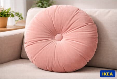 Coussin rond IKEA KRANSBORRE en velours rose sur canapé beige, avec logo IKEA en bas à droite.