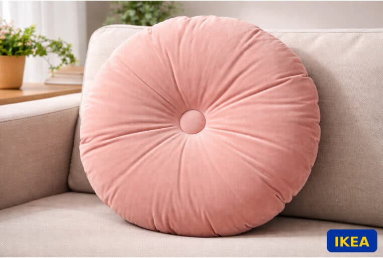 Coussin rond IKEA KRANSBORRE en velours rose sur canapé beige, avec logo IKEA en bas à droite.