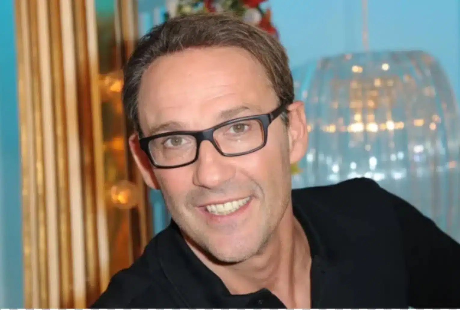 Portrait de Julien Courbet avec lunettes, sur fond bleu.