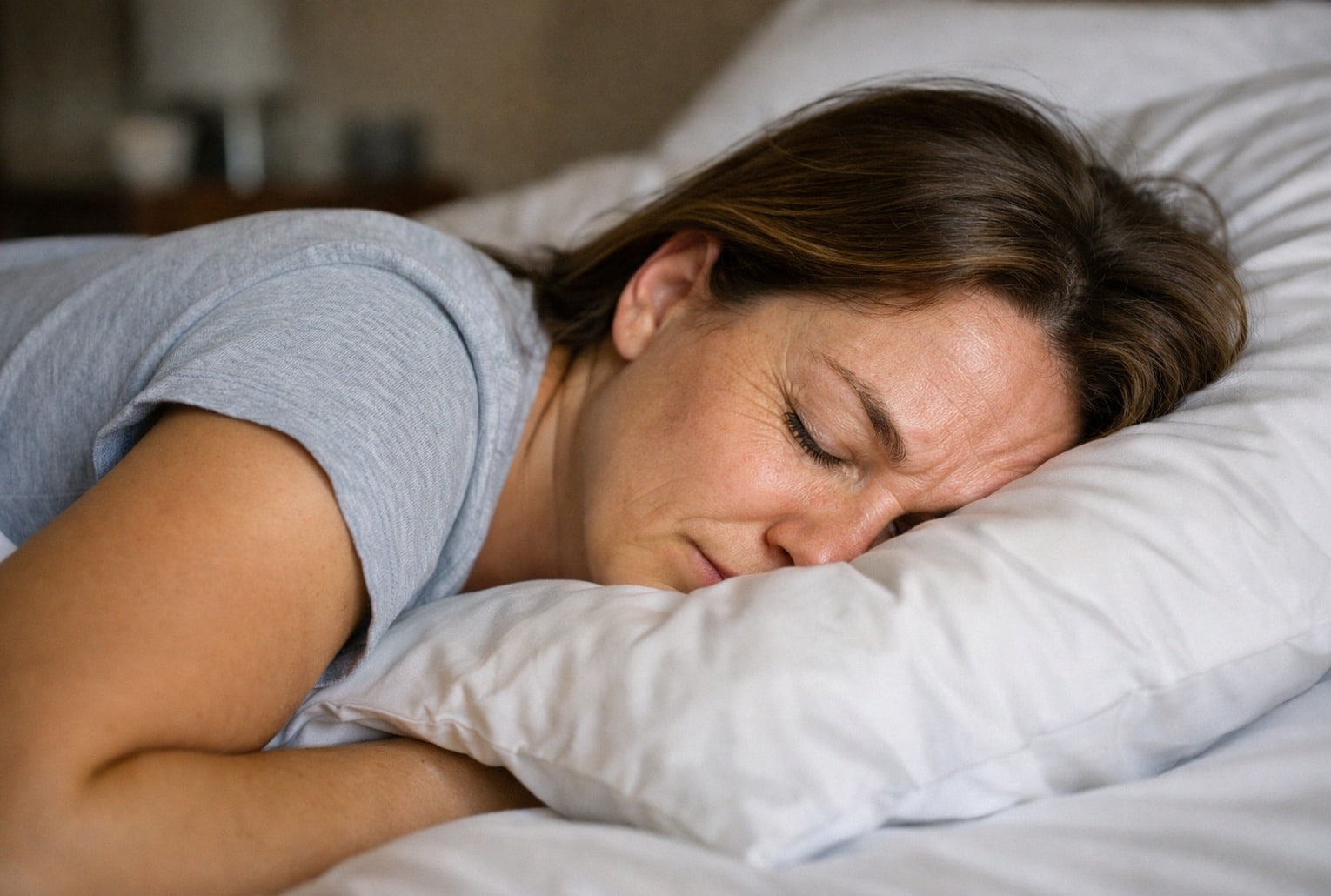 Position pour dormir rides : femme dormant sur le ventre, visage pressé contre un oreiller blanc.