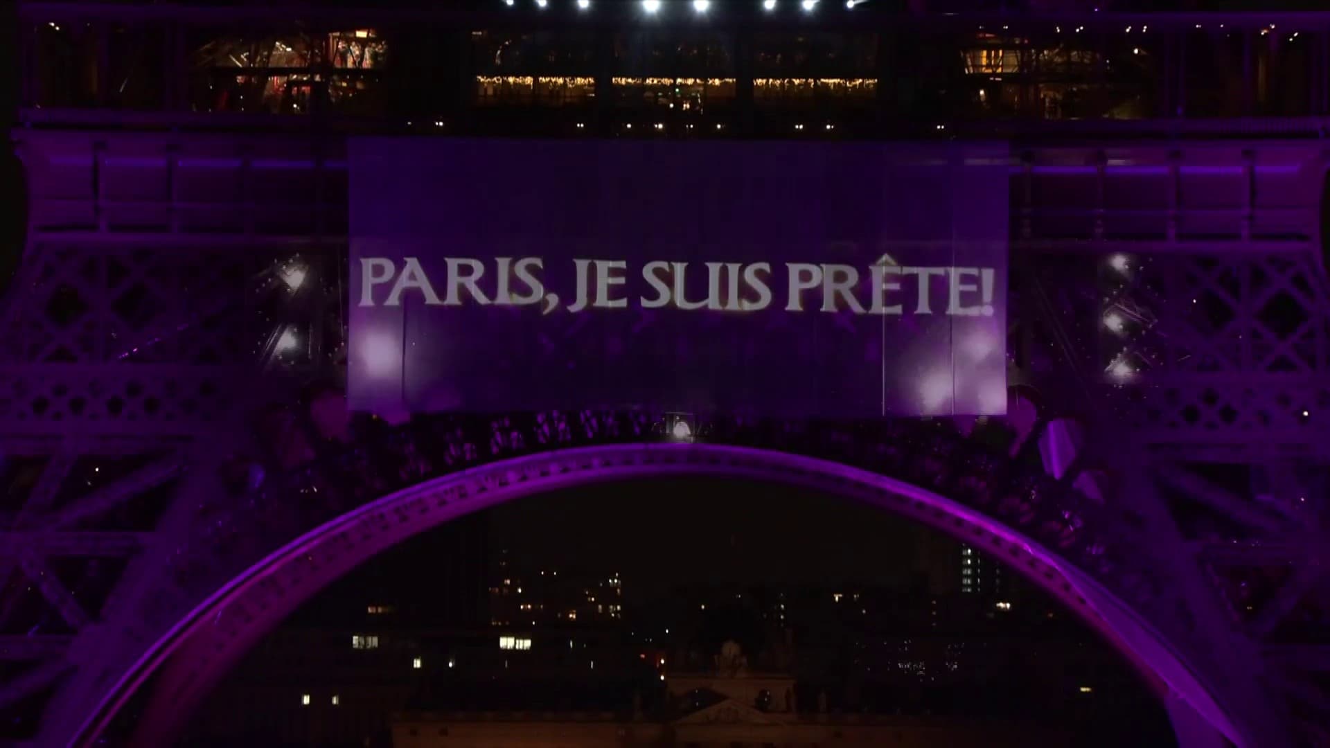 La Tour Eiffel est illuminée en violet avec une bannière affichant "PARIS, JE SUIS PRÊTE!".