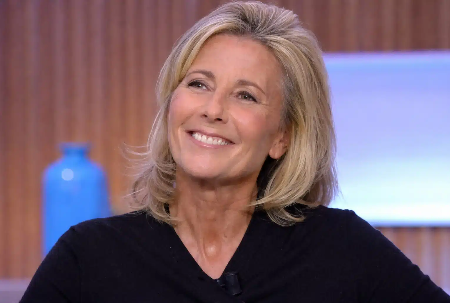 Claire Chazal souriante en studio, cadrage serré, fond flou aux tons bois et bleus