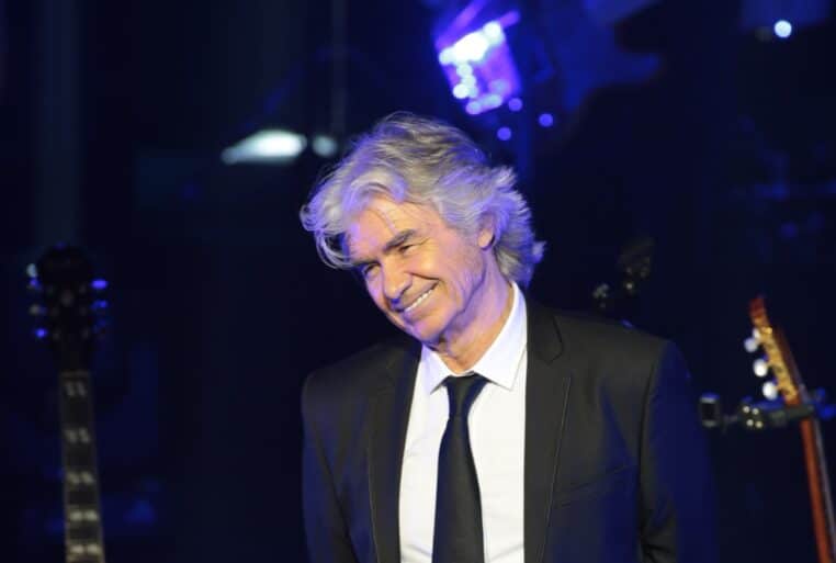 Daniel Guichard sur scène en costume noir sous un éclairage bleu lors d’un concert en 2015.