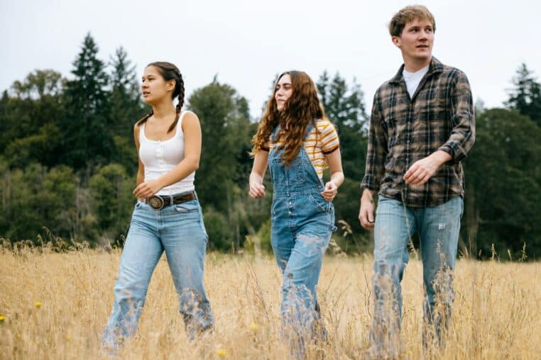 Three young people walk through a dry grassy field.