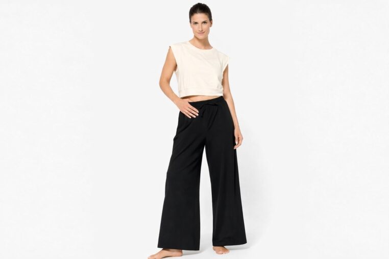 Femme portant le pantalon ample Domyos noir de Decathlon avec un top écru, sur fond neutre.