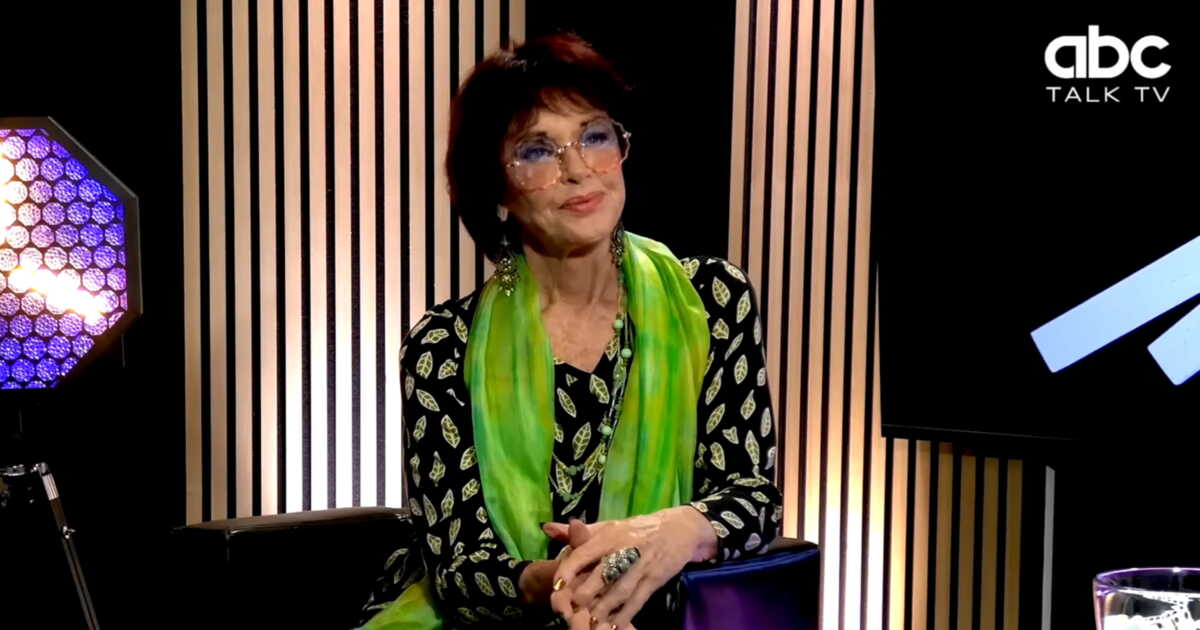 Anny Duperey en interview sur le plateau d'ABC Talk TV, portant une veste noire à motifs et un foulard vert
