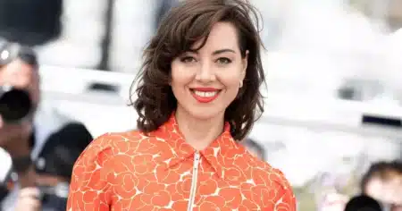 Aubrey Plaza souriante en robe orange à fleurs lors d'un événement public
