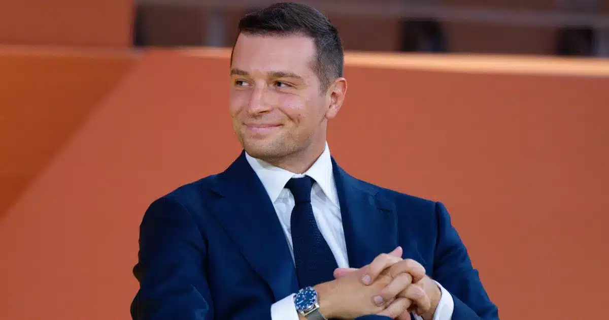 Jordan Bardella souriant en costume bleu marine lors d'un événement officiel