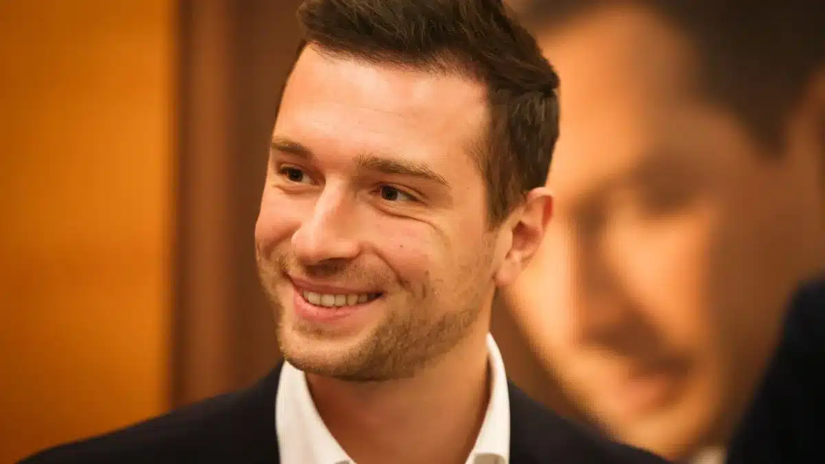 Jordan Bardella souriant lors d'un événement, regard tourné vers la droite
