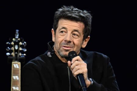 Patrick Bruel tenant un microphone sur scène, vêtu de noir, lors d'un concert