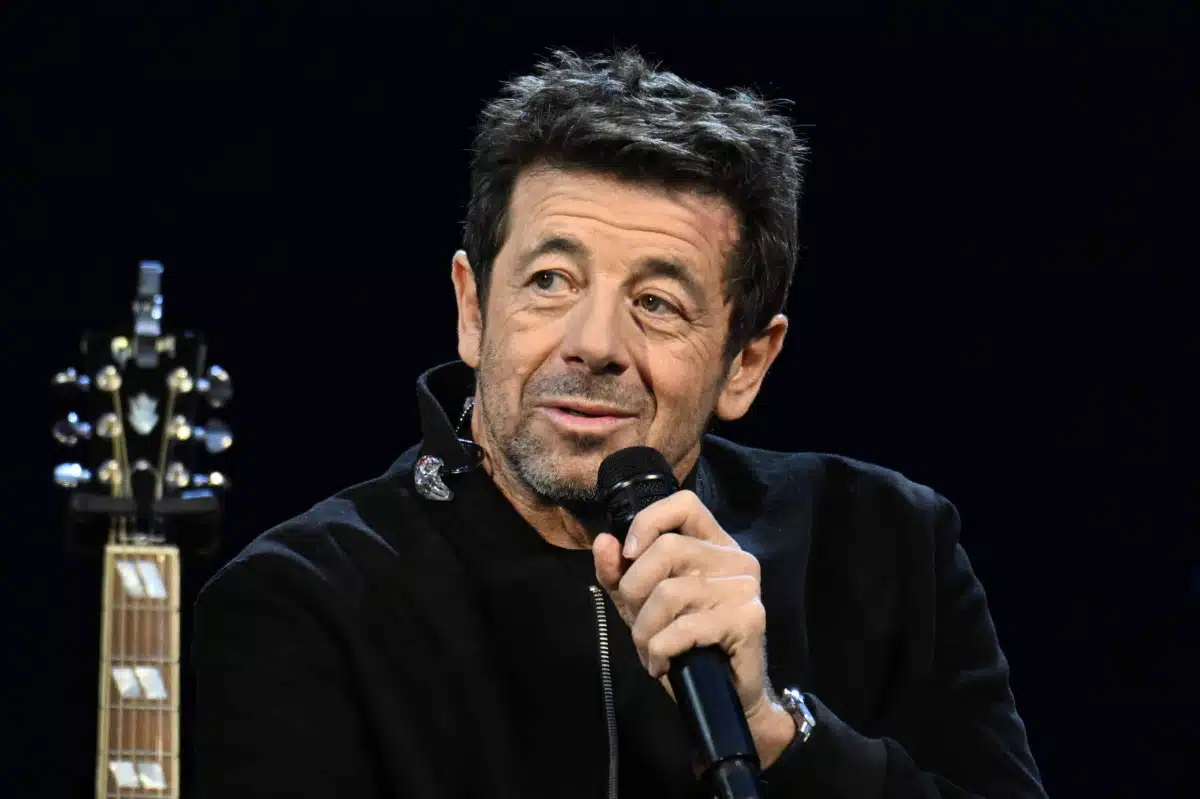 Patrick Bruel tenant un microphone sur scène, vêtu de noir, lors d'un concert