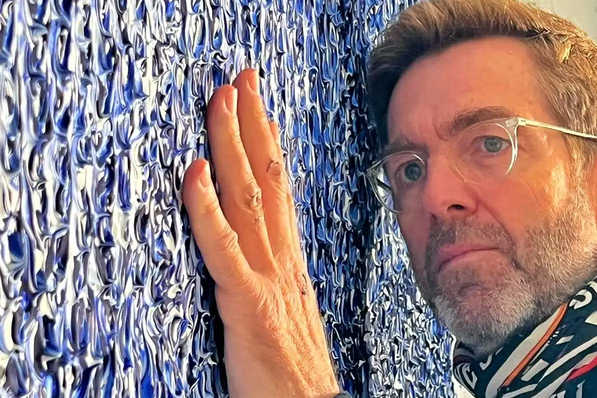 Alexandre Delpérier, ancien présentateur de Vidéo Gag, pose la main sur l'une de ses toiles texturées bleu et blanc dans son atelier