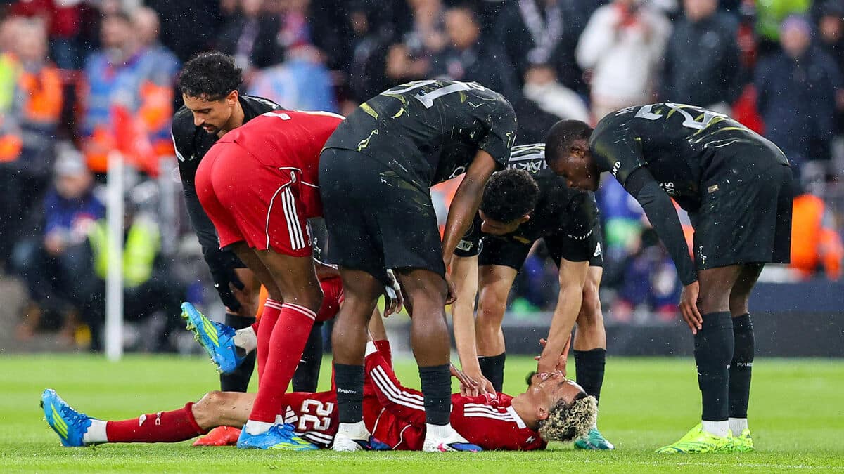 Hugo Ekitike allongé sur la pelouse d'Anfield, entouré de joueurs du PSG et de Liverpool qui se penchent vers lui après sa blessure