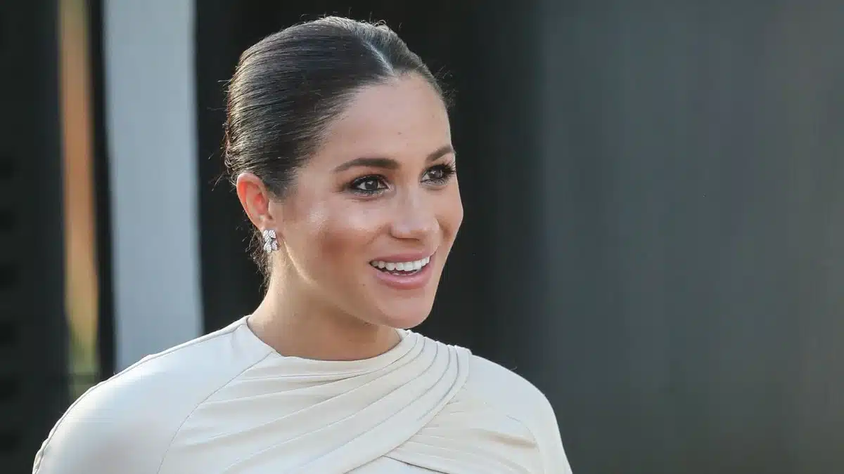 Meghan Markle souriante lors d'un événement officiel, vêtue d'une robe blanche