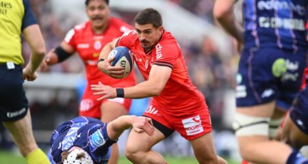 Antoine Dupont en maillot rouge et noir du Stade Toulousain tente de résister au plaquage d'un joueur de l'UBB lors du quart de finale de Champions Cup