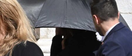Une silhouette dissimulée sous un grand parapluie noir à l'entrée de la cathédrale lors des obsèques de Loana à Nice