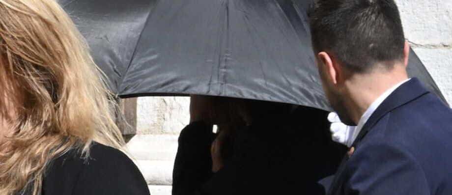 Une silhouette dissimulée sous un grand parapluie noir à l'entrée de la cathédrale lors des obsèques de Loana à Nice
