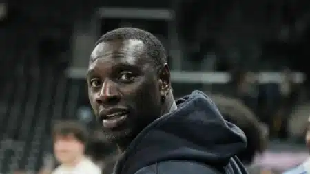 Omar Sy de profil, l'air pensif, dans un stade en arrière-plan