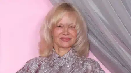 Pamela Anderson souriante sans maquillage, cheveux blonds courts, lors d'un événement mode