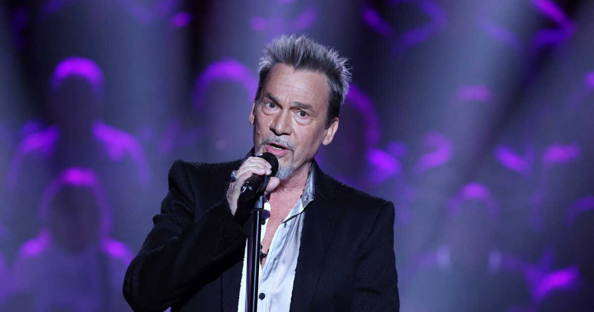 Florent Pagny chantant sur scène, micro en main, sous un éclairage violet lors de sa tournée