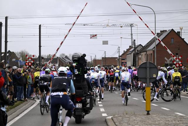 Le peloton du Tour des Flandres approchant à pleine vitesse un passage à niveau avec les barrières qui s'abaissent