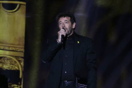 Patrick Bruel chantant sur scène avec un micro, vêtu en noir