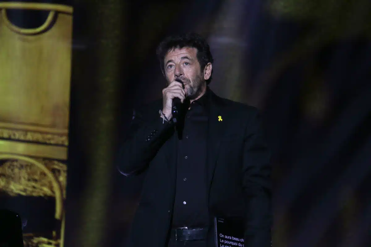 Patrick Bruel chantant sur scène avec un micro, vêtu en noir