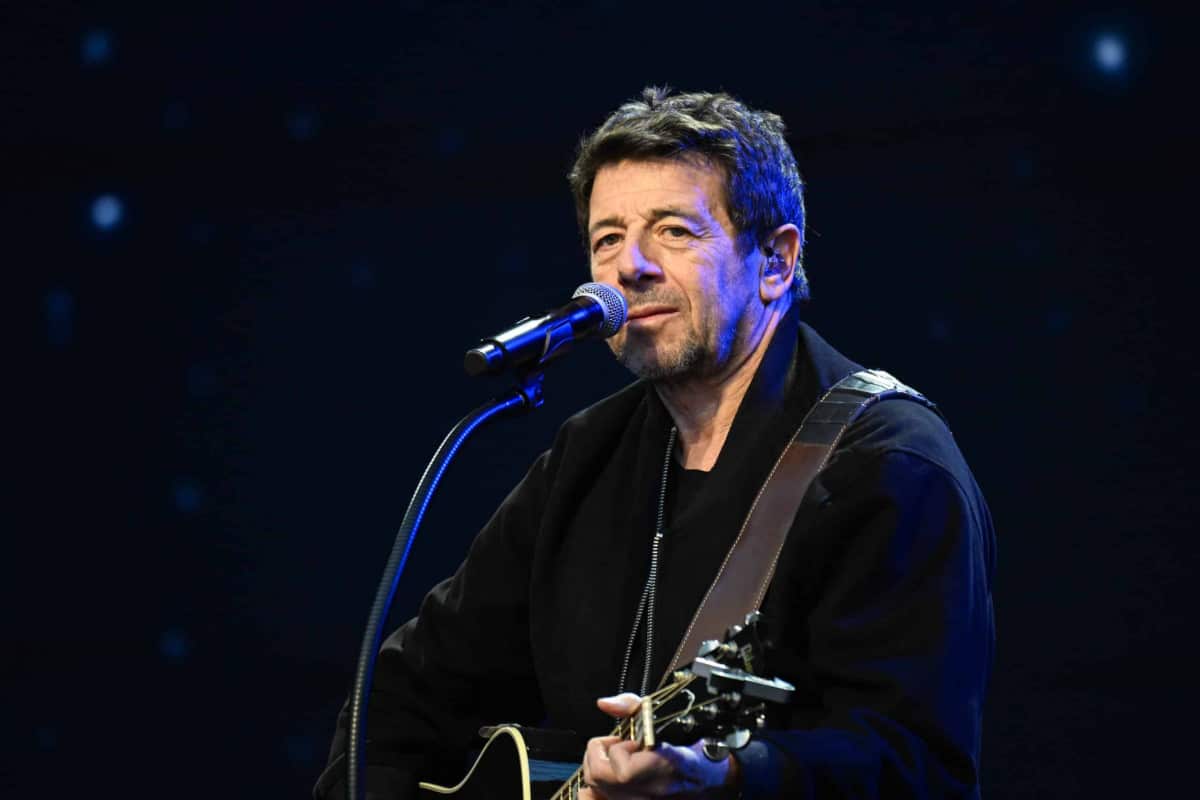 Patrick Bruel sur scène avec une guitare devant un microphone