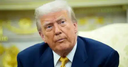 Donald Trump en gros plan, expression sérieuse, costume bleu et cravate dorée, à la Maison Blanche
