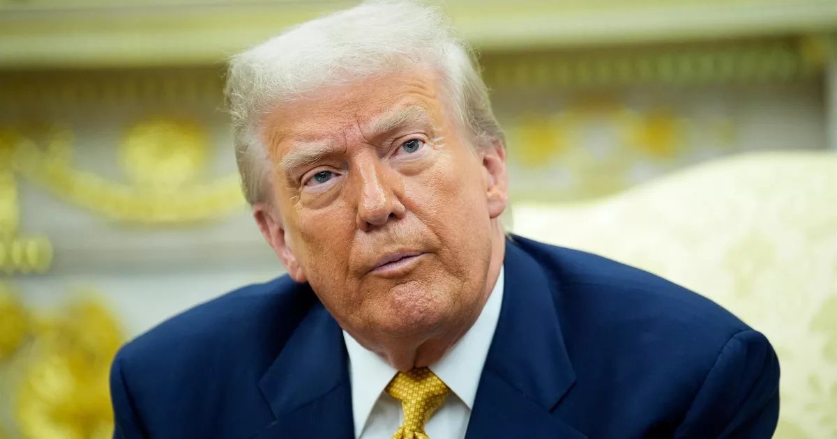 Donald Trump en gros plan, expression sérieuse, costume bleu et cravate dorée, à la Maison Blanche