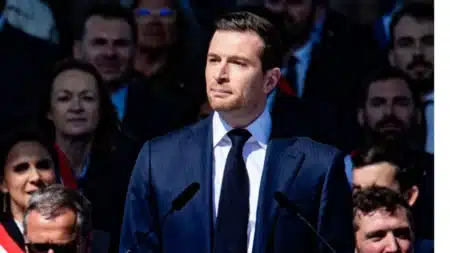 Jordan Bardella lors d'un discours officiel, en costume sombre, regard sérieux
