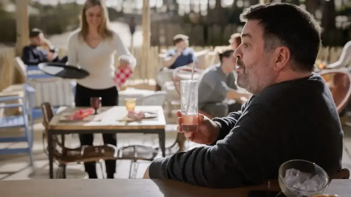 Un homme attablé en terrasse de restaurant tient un verre, regard tendu, dans un épisode d'Un si grand soleil