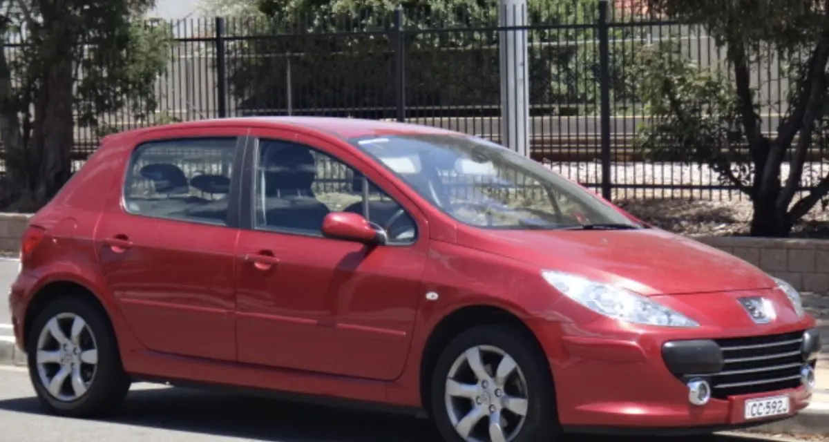 Une Peugeot 307 rouge garée dans une rue ensoleillée, symbole du choix modeste de Valentin Vacherot à Monaco