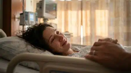 Femme allongée dans un lit d'hôpital, regard fragile et main tenue