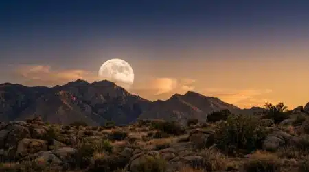 Pleine lune se levant derrière des sommets montagneux au crépuscule