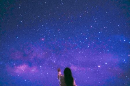 A silhouette of a person reaching towards a vivid starry night sky, featuring the Milky Way.