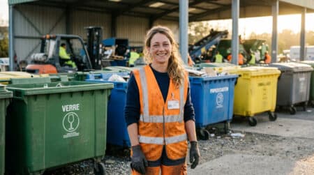 Opératrice de tri en gilet orange devant des conteneurs de recyclage