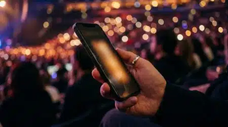 Smartphone tenu en main devant des lumières de concert floues